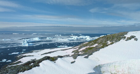 Wall Mural - Pristine Antarctic winter landscape in sunny day. Mountain rock glacier, icebergs, ice floes floating frozen polar ocean. Blue sky in background. Antarctica travel, explore wild nature. Aerial shot