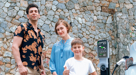 Wall Mural - Family road trip vacation with electric vehicle, lovely family recharge EV car with green and clean energy. Stone seawall background and eco friendly car travel for sustainable environment. Perpetual