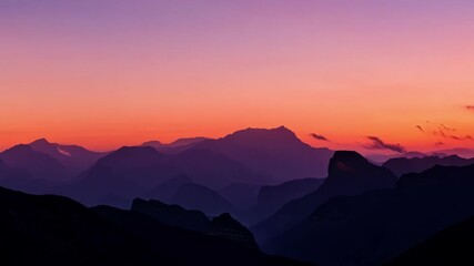 Sticker - The sky gradually transforms from a soft blue to fiery reds and oranges as the sun sinks into the horizon over the majestic mountains.