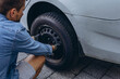 © Екатерина Лукашина - Young man in unscrewing lug nuts on car wheel in process of new tire replacement,using wrench while changing flat tire on the road.
