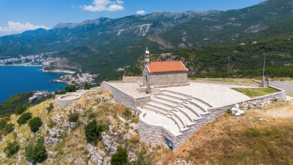 Wall Mural - Aerial view of St Sava church overlooking Sveti Stefan, a medieval village located on a small island in the bay of Budva along the Adriatic Coast, Montenegro