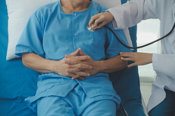 Wall Mural - Doctor using stethoscope to listen senior man heart during examination in hospital room and wearing visor as safety precaution against coronavirus. Medical control for infections, disease.