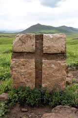 Sticker - Cross-shaped stone monument in grassy field with mountains in background