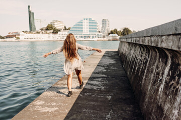 Wall Mural - woman in a white dress is walking on a pier near the water. The scene is peaceful and serene, with the woman's long hair blowing in the wind.