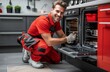 © Georgii - Smiling repairman in red overalls fixing an oven in a modern kitchen