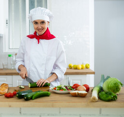 Portrait of positive woman chef cutting vegetables for salad