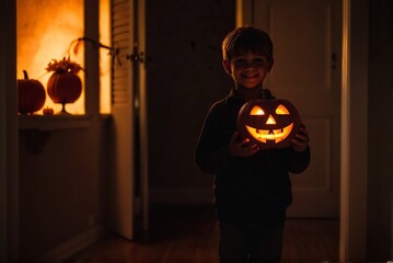 A happy kid holding Jack O Lantern in his house at night for the celebration of Halloween with copy space.