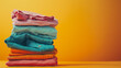 © VK Studio - A vibrant stack of neatly folded clothes in various bright colors against a yellow background, creating a sense of warmth and organization.