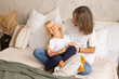 © Marharyta - Mother and her little son sitting on bed at home having a good time wearing white t-shirts