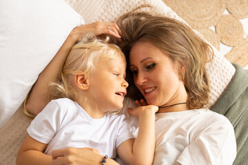 Portrait of happy laughing mother and her little child son baby boy hugging lying on bed at home. Motherhood, affection