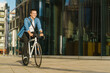 © muse studio - A man riding a bicycle past modern glass buildings, smiling in the warm sunlight, embodying urban commute.