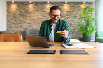 Wall Mural - smiling male accountant paying bills with credit card over computer while sitting at desk in office