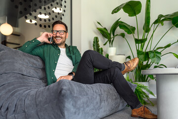 Wall Mural - low angle view of confident businessman discussing with client over mobile phone on sofa in office