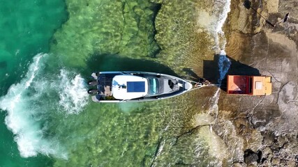 Wall Mural - Aerial drone top view still video of speed boat on trailer being towed by truck from emerald exotic sea to land