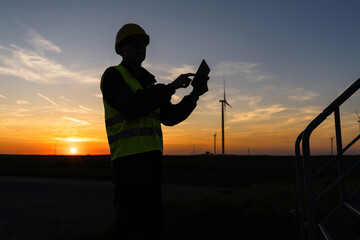 Aufkleber - Engineer with digital tablet works on a field of wind turbines at sunset.