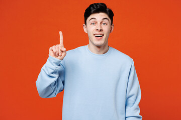 Wall Mural - Young smiling happy Caucasian man he wears blue sweatshirt casual clothes holding index finger up with great new idea isolated on plain red orange color background studio portrait. Lifestyle concept.