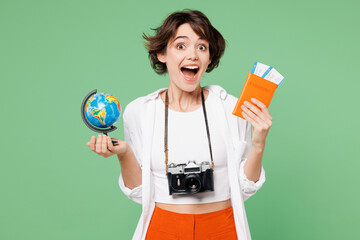 Wall Mural - Traveler happy surprised shocked woman wear casual clothes hold passport ticket globe isolated on plain green background. Tourist travel abroad in free spare time rest getaway Air flight trip concept