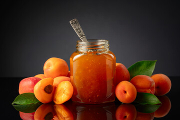 Wall Mural - Apricot jam in glass jar and fresh fruits on a black reflective background.