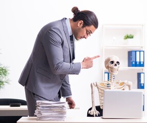 Wall Mural - Young male employee and skeleton in the office