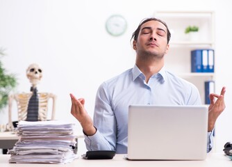 Wall Mural - Young male employee and skeleton in the office