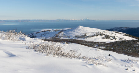 Wall Mural - Mountain landscape. View from the snowy mountainside to the sea coast. In the foreground are bushes and white snow. The Sea of Okhotsk is in the distance. Cold weather. Magadan region, Russia.