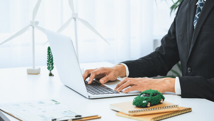 Businessman working in office developing plan or business project on eco-friendly ev car using net zero alternative energy technology on computer for greener environment as apart of CSR effort. Gyre