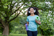 © Liubomir - Young African American athlete walking in park holding yoga mat and water bottle. Wearing headphones and smiling confidently. Outdoor fitness and healthy lifestyle concept.