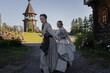 © Ulia Koltyrina - Young women in folk costume run forward holding hands in a village among wooden architecture, Slavic or Nordic style