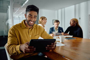 Four happy young multiracial adults in businesswear talking at meeting with digital tablet at office