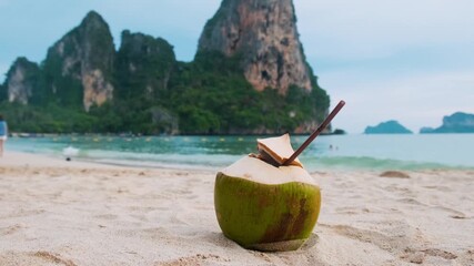 Canvas Print - Coconut water drink with a straw on sandy tropical Railay beach with turquoise water and rock formations in Krabi province, Thailand. Refreshment summer drink