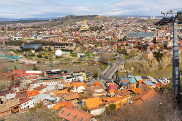 Wall Mural - Spring cityscape of historical area of Tbilisi with view of modern bow-shaped bridge across Mtkvari River, two tubular metallic structures of Rike concert hall and white hot air balloon, Georgia