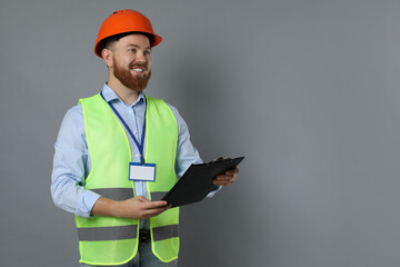 Engineer in hard hat with clipboard on grey background, space for text