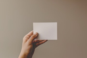 Hand holding a blank white card against a plain background.