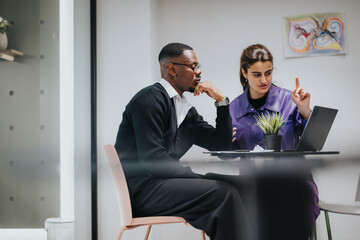 Wall Mural - African American man and Indian woman discuss work, engrossed in a collaborative effort in a bright, contemporary office space.