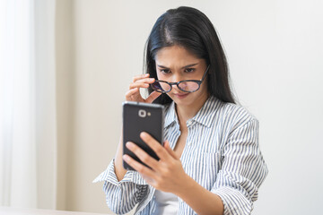 Wall Mural - Presbyopia, Hyperopia middle aged asian woman holding eyeglasses problem with vision blurred ,trying to read text message from smart mobile phone screen, eye disease of old, eyesight farsightedness.