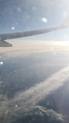 Wall Mural - View through the window glass with glare on it to the wing of an airplane against the backdrop of the rising sun above the clouds. Vertical footage, 21 seconds. Flight over the earth at sunrise