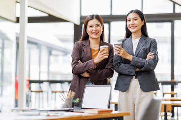 Wall Mural - Two young asian women holding digital tablet and working in modern office
