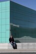© Adobe Contributor - Man Sitting On A Wall In Front Of A Green Building