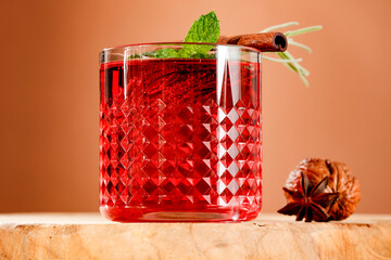 Sticker - Red mulled wine in glass with fresh rosemary and mint and cinnamon stick on wooden table with walnut and spice clove and brown wall background.