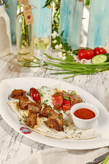 Wall Mural - Pork Shashlik with Lavash, Sauce, and Vegetable Salad under Sunlight on Wooden Table