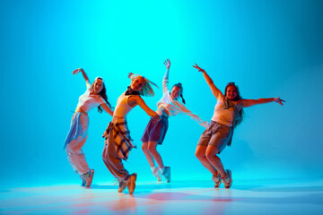 Group of artistic dancers, dressed in casual attire, pose confidently under vibrant blue lighting, highlighting expressive hip-hop moves. Concept of music, fashion and art, movement, sport and hobby.