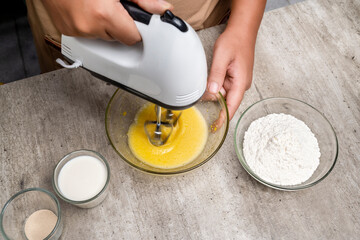 A person is making a cake and has a bowl of flour and sugar on the table