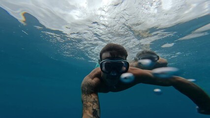 Wall Mural - Beautiful and cute couple of millennials young people snorkeling and diving together looking underwater for fishes and coral having fun and enjoying. Summer time swimming in the sea blue ocean.
