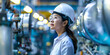 © Aigo labs - A young female engineer wearing a white helmet and safety goggles stands in a modern industrial factory, surrounded by machinery.