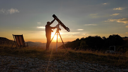 Wall Mural - Amateur astronomer looking at the evening skies, observing planets, stars, Moon and other celestial objects with a telescope just before sun down.