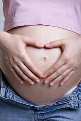 Wall Mural - Female on 6th month of pregnancy. Woman touching with hands her naked belly and shows heart sign.