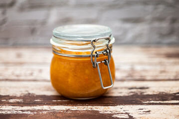 Glass jar on a wooden table with delicious homemade orange jam inside. Homemade orange jam sweet break.