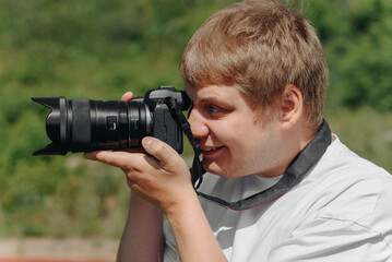 dslr camera in hands, young adult caucasian photographer in white t-shirt at work outdoors in sunny summer day, looking left and taking picture