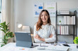 © Wasana - Young asian businesswoman sitting with arms crossed at office desk