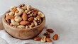 © pinporn manosri - A wooden bowl of mixed nuts on a linen napkin, with a light grey background emphasizing their natural beauty